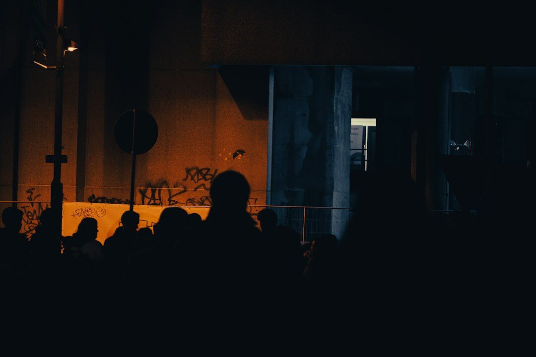 Silhouettes of a diverse audience watching a stage from behind in dim light