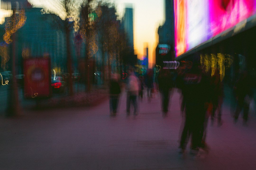 Blurred pedestrians passing illuminated digital screens in a city street at dusk